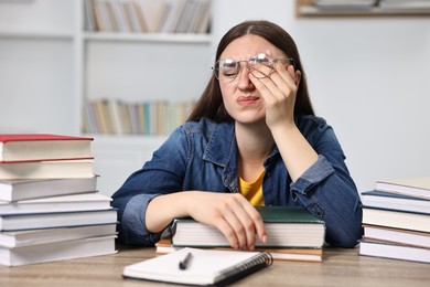 Photo of Overwhelmed student before exam at table among books indoors