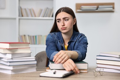 Photo of Overwhelmed student before exam at table among books indoors