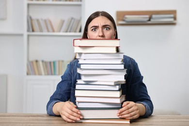 Overwhelmed student before exam with stack of books at table indoors