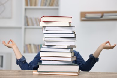 Photo of Student meditating before exam behind stack of books at table indoors