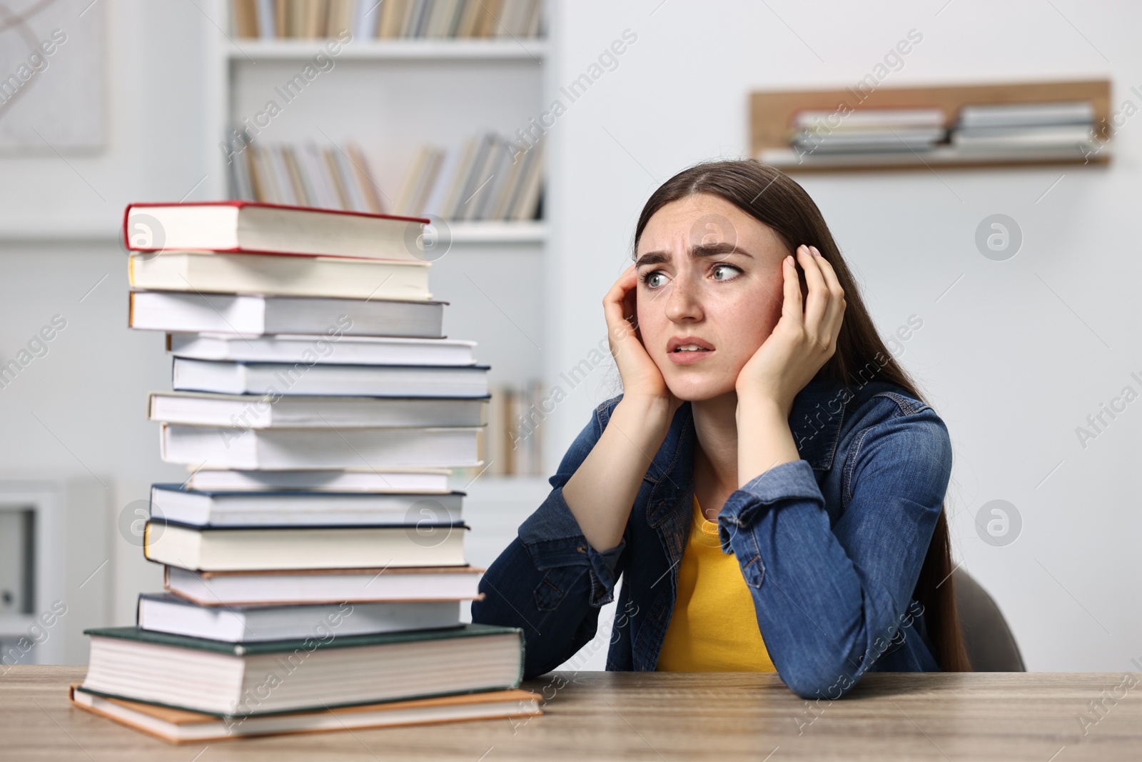 Photo of Overwhelmed student before exam at table among books indoors