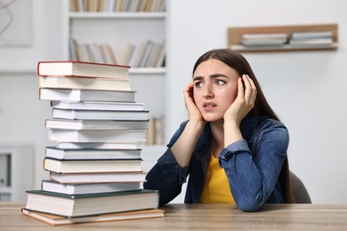 Overwhelmed student before exam at table among books indoors