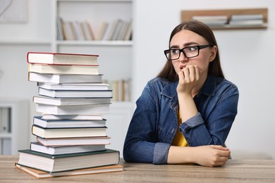 Overwhelmed student before exam at table among books indoors