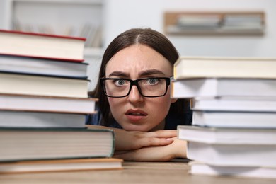 Worried student before exam at table among stacks of books indoors