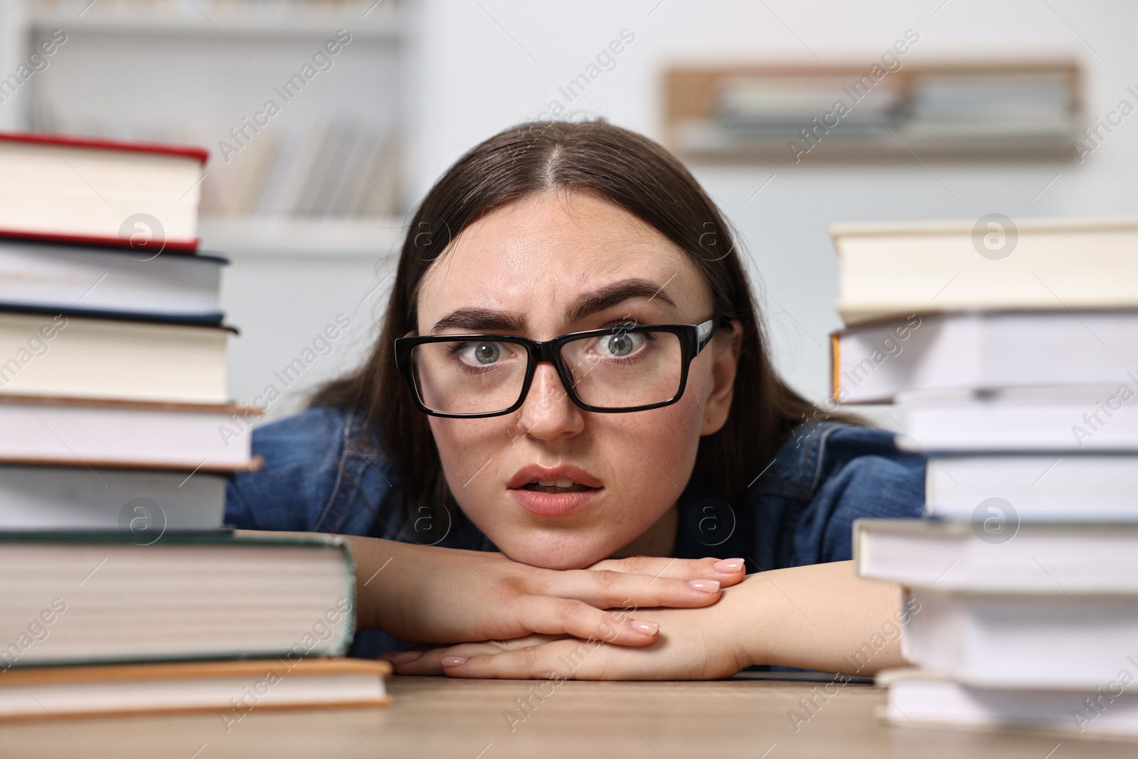 Photo of Worried student before exam at table among stacks of books indoors