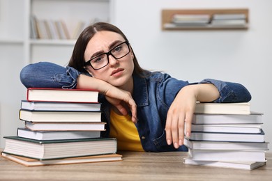 Photo of Tired student before exam at table among stacks of books indoors