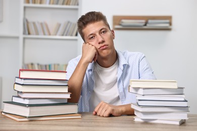 Tired student before exam at table among stacks of books indoors