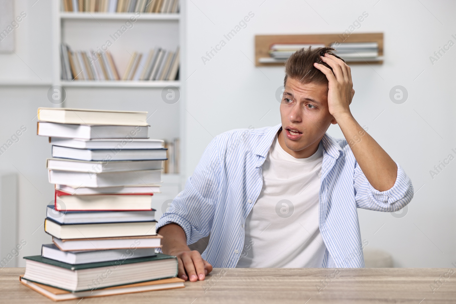 Photo of Excited student before exam looking at stack of books at table indoors