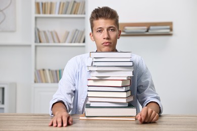 Photo of Tired student before exam with stack of books at table indoors