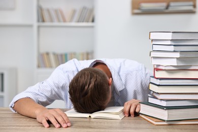 Tired student before exam with stack of books at table indoors