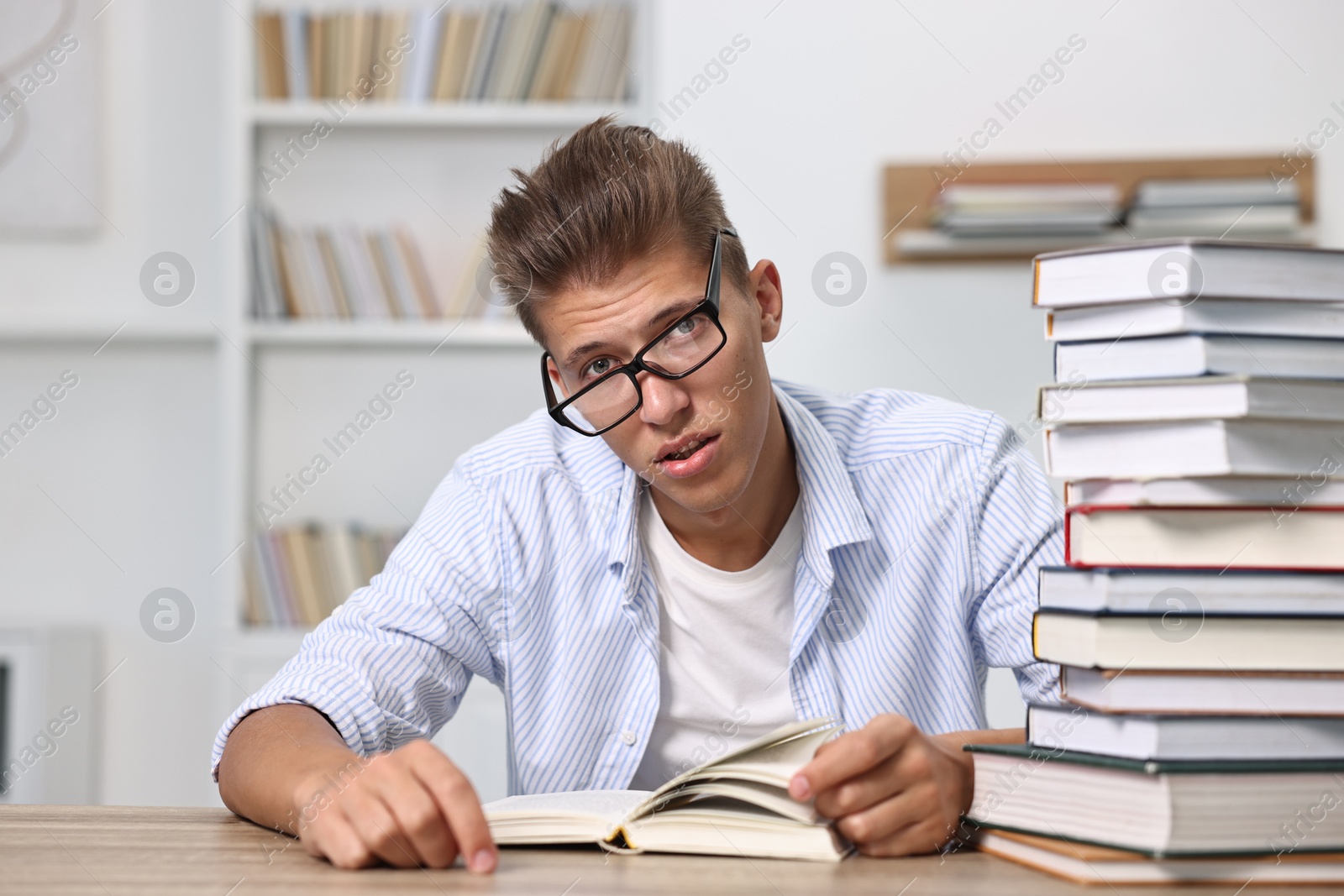 Photo of Tired student before exam at table with stack of books indoors