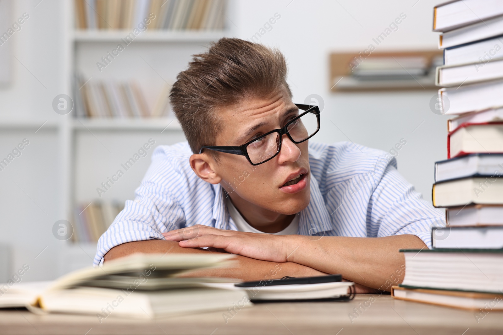 Photo of Tired student before exam with stack of books at table indoors