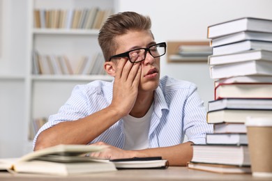 Tired student before exam with stack of books at table indoors