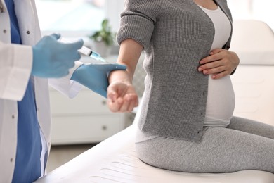 Doctor giving injection to pregnant woman at hospital, closeup