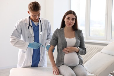 Doctor giving injection to smiling pregnant woman at hospital