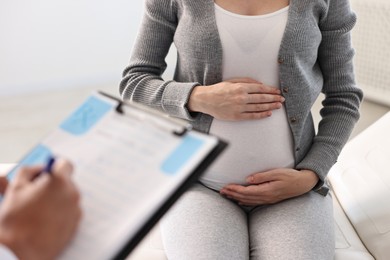 Doctor with clipboard consulting pregnant patient in clinic, closeup