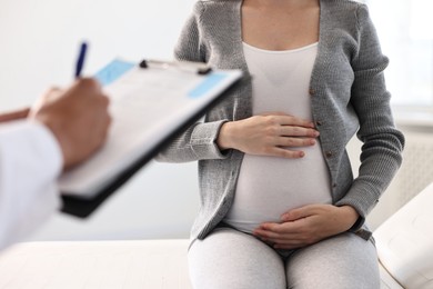 Photo of Doctor with clipboard consulting pregnant patient in clinic, closeup