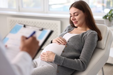 Photo of Doctor with clipboard consulting pregnant patient in clinic, closeup