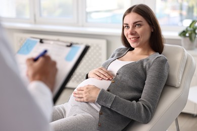 Photo of Doctor with clipboard consulting smiling pregnant patient in clinic, closeup