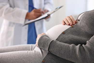 Doctor with clipboard consulting pregnant patient in clinic, closeup