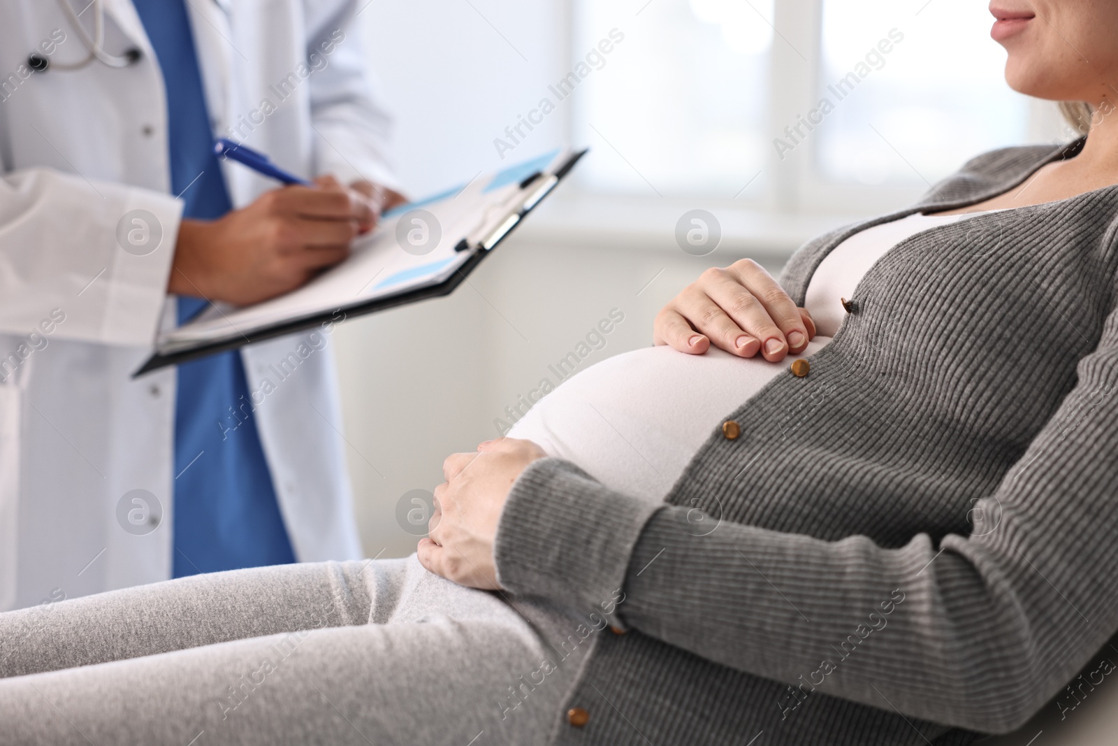 Photo of Doctor with clipboard consulting pregnant patient in clinic, closeup