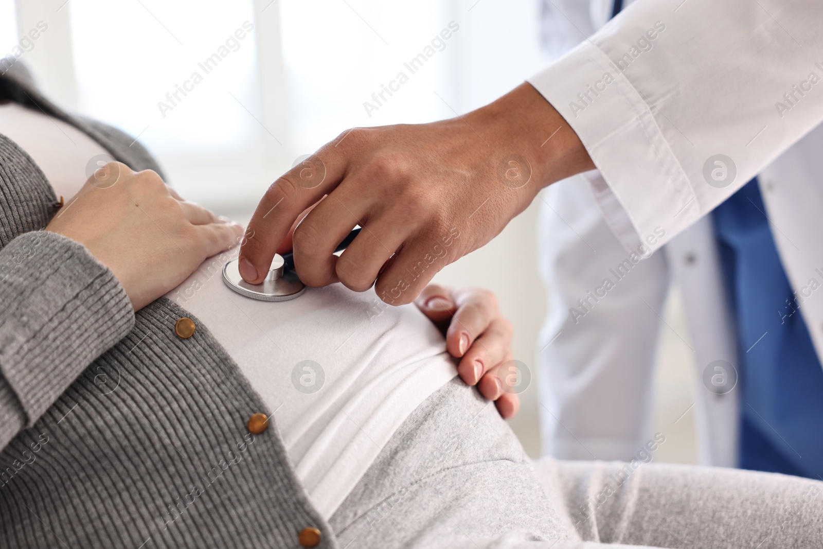 Photo of Pregnancy checkup. Doctor with stethoscope listening baby's heartbeat in patient's tummy indoors, closeup