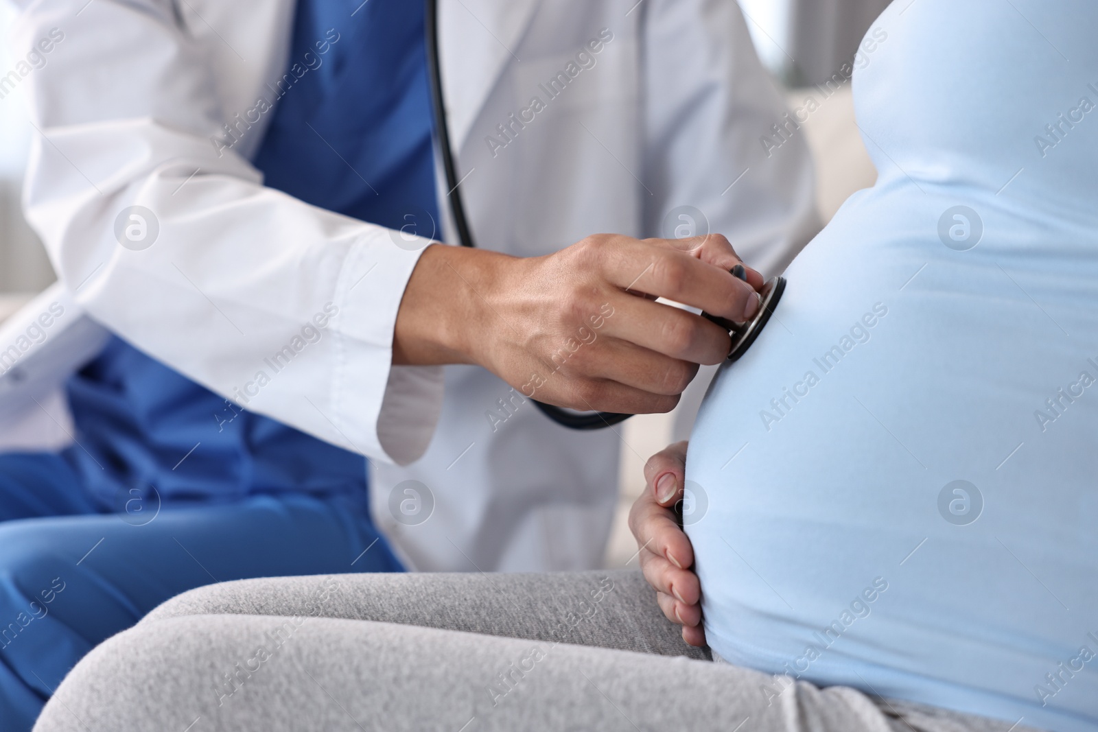 Photo of Pregnancy checkup. Doctor with stethoscope listening baby's heartbeat in patient's tummy indoors, closeup