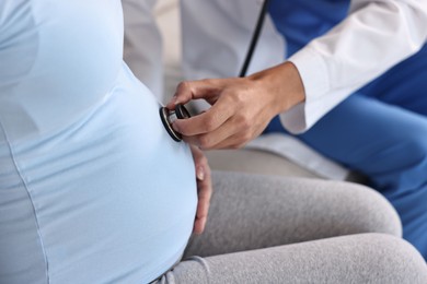 Photo of Pregnancy checkup. Doctor with stethoscope listening baby's heartbeat in patient's tummy indoors, closeup