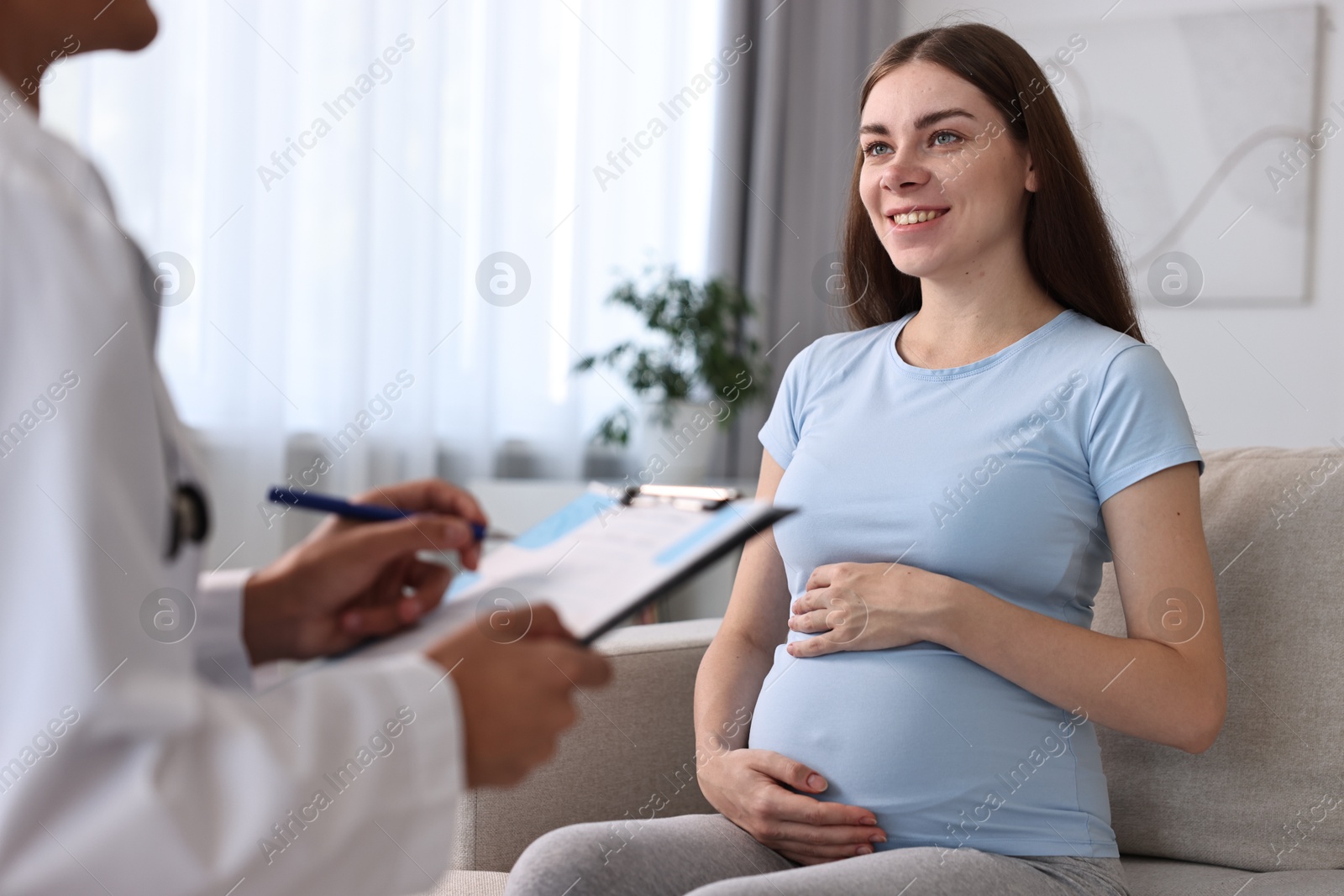 Photo of Doctor with clipboard consulting smiling pregnant patient indoors, closeup