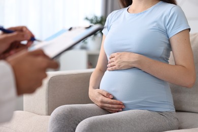 Photo of Doctor with clipboard consulting pregnant patient indoors, closeup