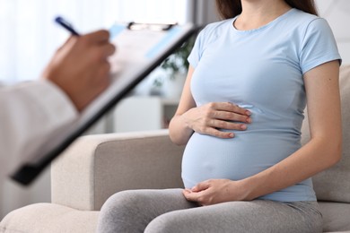 Doctor with clipboard consulting pregnant patient indoors, closeup