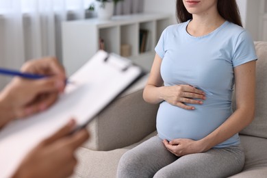 Doctor with clipboard consulting pregnant patient indoors, closeup