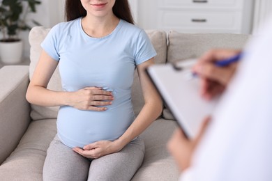 Doctor with clipboard consulting pregnant patient indoors, closeup