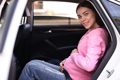 Smiling pregnant woman with safety belt in car