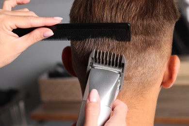 Photo of Professional barber making stylish haircut in salon, closeup