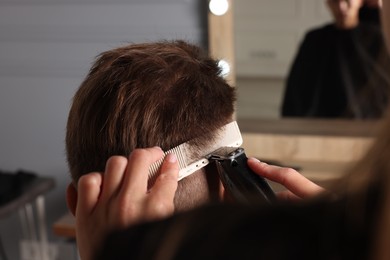 Photo of Professional barber making stylish haircut in salon, closeup