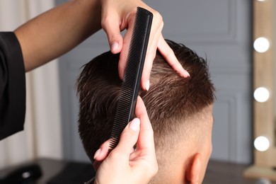 Photo of Hair cutting. Hairdresser combing man's hair in barbershop, closeup