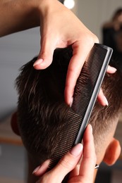 Hair cutting. Hairdresser combing man's hair in barbershop, closeup