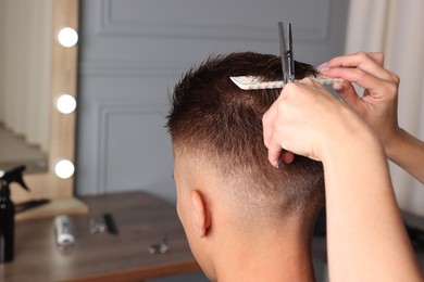 Professional hairdresser cutting client's hair with scissors in barbershop, closeup