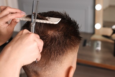 Professional hairdresser cutting client's hair with scissors in barbershop, closeup