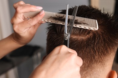 Professional hairdresser cutting client's hair with scissors in barbershop, closeup