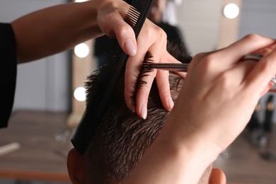 Professional hairdresser cutting client's hair with scissors in barbershop, closeup