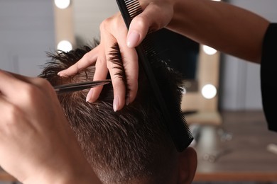 Professional hairdresser cutting client's hair with scissors in barbershop, closeup