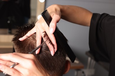 Photo of Professional hairdresser cutting client's hair with scissors in barbershop, closeup