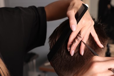 Professional hairdresser cutting client's hair with scissors in barbershop, closeup