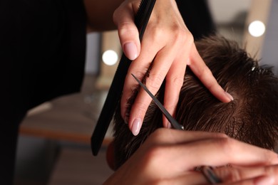 Photo of Professional hairdresser cutting client's hair with scissors in barbershop, closeup