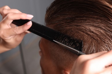 Photo of Professional hairdresser cutting client's hair with scissors in barbershop, closeup