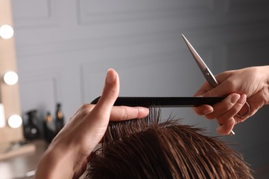 Photo of Professional hairdresser cutting client's hair with scissors in barbershop, closeup