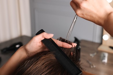 Photo of Professional hairdresser cutting client's hair with scissors in barbershop, closeup