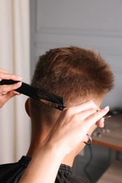 Professional hairdresser cutting client's hair with scissors in barbershop, closeup